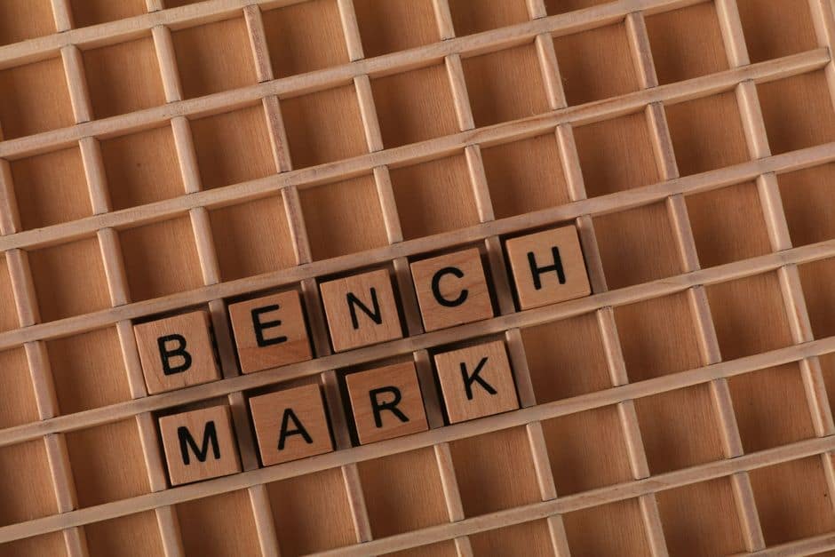 Dashboard de benchmark de código (Terminal Bench 3.0) num monitor ultrawide, gráficos de barras a subir, estética dark mode com acentos verdes, still life tech editorial, sem pessoas.