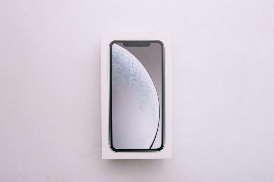 Still life editorial tech: smartphone e laptop sobre mesa minimalista exibindo dashboard de API com gráfico de preços em queda, fundo em tons de azul e branco, macro shot do ecrã com código e métricas de tokens, sem pessoas